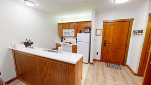 A compact kitchen with wooden cabinets, a white countertop, a microwave, a stove, and a refrigerator. - AS 141: Pool-Level King Bed | Ski-In/Out | Village Center (Snowshoe)