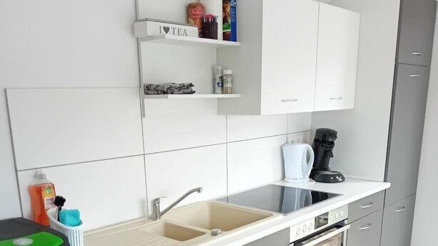 Een moderne keuken met grijze kastjes, een wit aanrecht, een spoelbak, een koffiezetapparaat en een prullenbak.