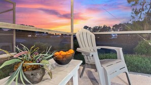 A balcony with a view of a sunset, a chair, a table with a bowl of oranges, and a potted plant. - Stylish 3BR, Pool, Golf Views, Disney and Legoland (Haines City)