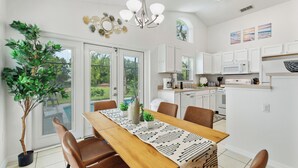 A dining area with a wooden table, chairs, a chandelier, and a potted plant. - Stylish 3BR, Pool, Golf Views, Disney and Legoland (Haines City)