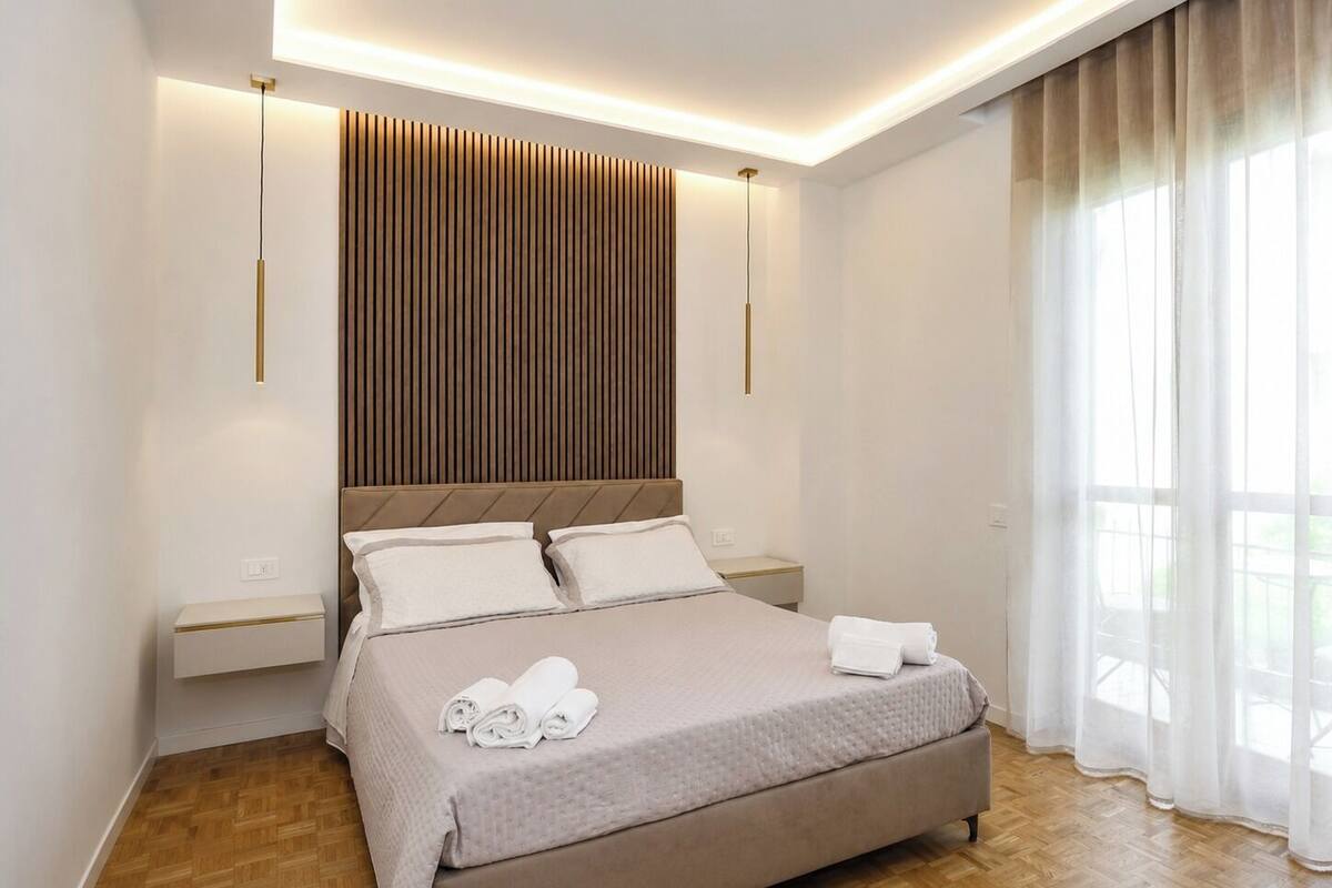 Ein modernes Schlafzimmer mit einem großen Bett, Nachttischen, einer Holzwand und einem Fenster mit Vorhängen.