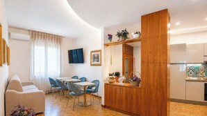 A modern living room with a sofa, dining area with chairs, a kitchen with cabinets, and a wooden partition. - Casa Lucia (Cava de' Tirreni)