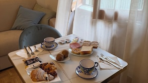 A dining table with breakfast items, a sofa, and a window with curtains. - Casa Lucia (Cava de' Tirreni)