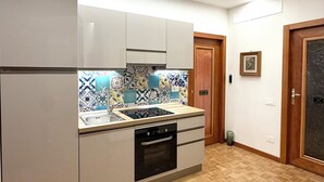 A modern kitchen with white cabinets, a patterned backsplash, and a herringbone wood floor. - Casa Lucia (Cava de' Tirreni)