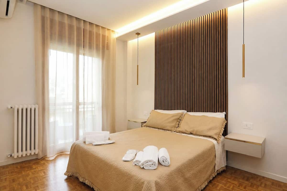 Ein Hotelzimmer mit einem Bett, einem Nachttisch, einem Heizkörper und einem Fenster mit Vorhängen.