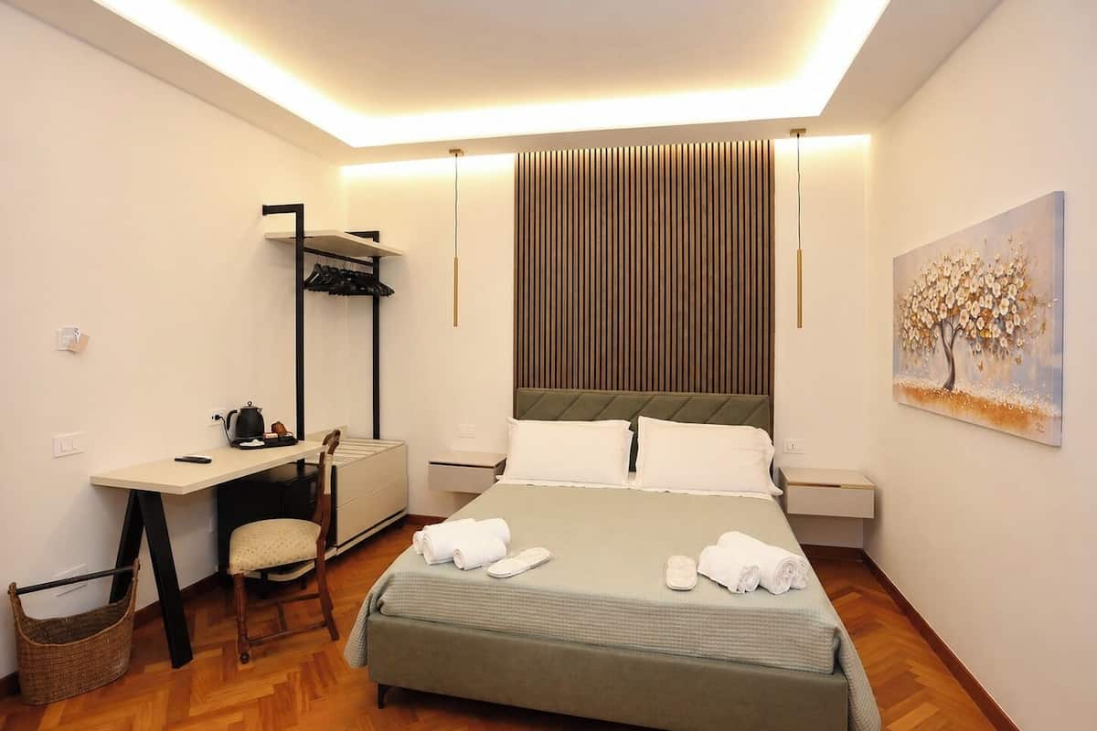 Ein Hotelzimmer mit einem Bett, einem Schreibtisch, einem Stuhl, einer Wandablage und einem Gemälde.