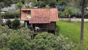 Uma pequena cabana de madeira com telhado de telhas, rodeada por vegetação exuberante e um cenário montanhoso.