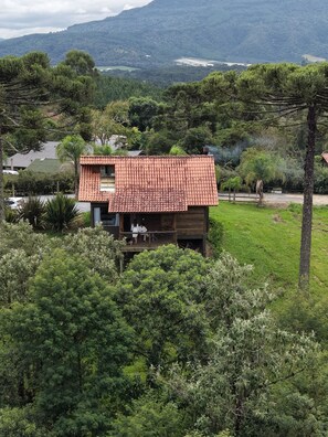 A small wooden cabin with a tiled roof, surrounded by lush greenery and a mountainous backdrop. - Pousada Trinca Ferro (Bom Retiro)