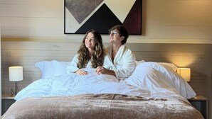 Une chambre avec un plafond en bois, un lit recouvert de draps blancs, un grand tableau abstrait accroché au mur et des lampes de chevet.