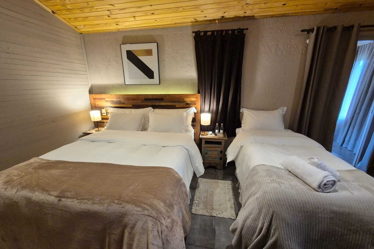 Une chambre d’hôtel avec deux lits, un plafond en bois, une tête de lit, une table de chevet, une lampe et un panneau fixé au mur.
