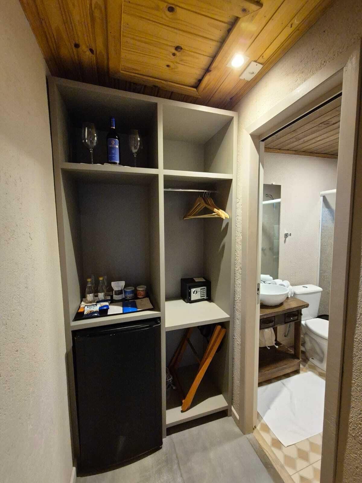 A compact room with a built-in mini-fridge, a small sink, and a shower. There are shelves with bottles and a radio.