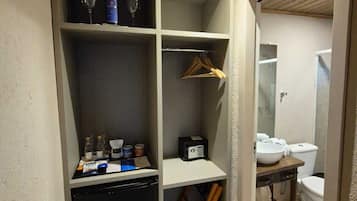 A compact room with a built-in mini-fridge, a small sink, and a shower. There are shelves with bottles and a radio.