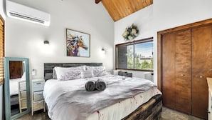 Ein Schlafzimmer mit einem Bett, einem hölzernen Kopfteil, einem Spiegel, einem Fenster mit Jalousien und einem Holzschrank.