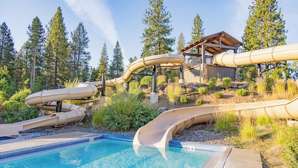 Ein Pool mit mehreren Wasserrutschen, einer Holzterrasse und einem Gebäude mit Dachkonstruktion.