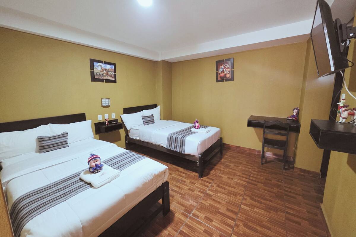 Ein Hotelzimmer mit zwei Betten, einem Schreibtisch, einem Sessel, einem Fernseher und zwei gerahmten Bildern an den Wänden.