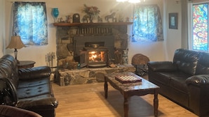 Una sala de estar acogedora con chimenea, sofás de cuero, techo de madera y un ventilador.