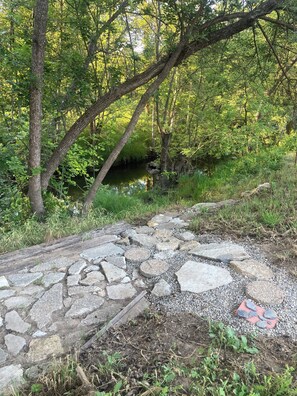 Ein Kiesweg führt durch ein bewaldetes Gebiet mit einem kleinen Bach.