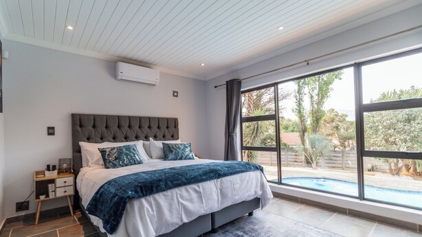 A bedroom with a large bed, a nightstand, a window with a view of a swimming pool, and an air conditioning unit on the wall.