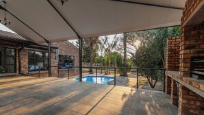 An outdoor patio area with a swimming pool, brick walls, and a covered seating area.