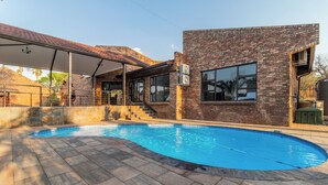 A swimming pool with a brick building, a covered patio, and a staircase leading to the building.
