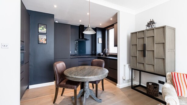 A modern kitchen with dark walls, a round dining table, and a cabinet with a unique design. - Elegant 2BR Belgravia Flat w/ Lift | Near Victoria (London)