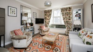A living room with a sofa, armchair, ottoman, television, and a patterned rug. - Elegant 2BR Belgravia Flat w/ Lift | Near Victoria (London)