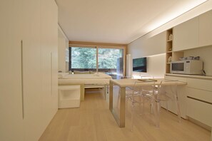 Ein gemütlicher Raum mit Bett, Esstisch mit Stühlen, Fernseher und Mikrowelle.