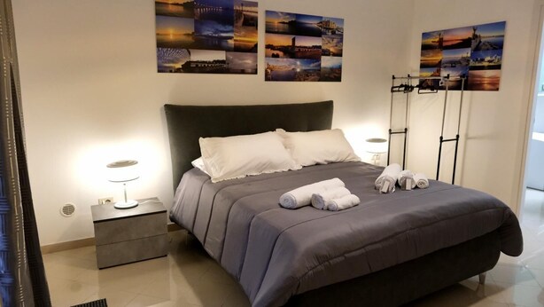Una habitación de hotel moderna con una cama grande, una mesita de noche, una lámpara de noche y una pared decorada con fotografías de paisajes.