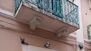 Entrada de edificio con puerta negra, un pequeño balcón con barandillas verdes y el número '179' en la pared.