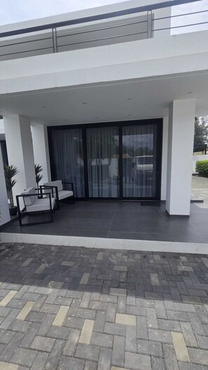 Ein modernes Gebäude mit überdachter Terrasse, großen Glasschiebetüren und einer Sitzgruppe mit Stühlen und Tisch.