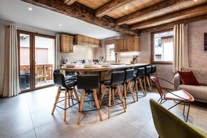 Eine moderne Küche mit Holzausstattung, einer zentralen Kochinsel mit Sitzgelegenheiten und einem Essbereich mit Tisch und Stühlen.