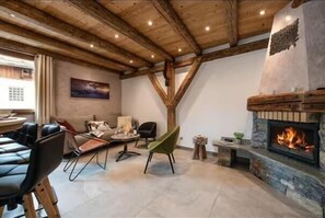 Ein Zimmer mit Kamin aus Stein, Holzbalken, einem Essbereich und einem grünen Stuhl.