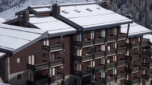 Um edifício moderno de vários andares com telhado coberto de neve, varandas e base de pedra.