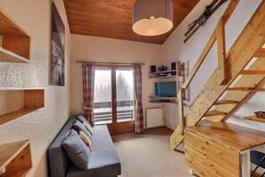 Ein gemütliches Zimmer mit einer Holztreppe, einem Sofa, einem Fernseher und einem Fenster mit Vorhängen.