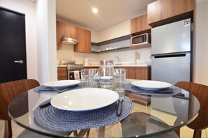 A modern kitchen with a glass dining table, wooden chairs, and a microwave. - Stay in Obispado! Security 24/7 4 beds 2BR2br 6ppl (Monterrey)