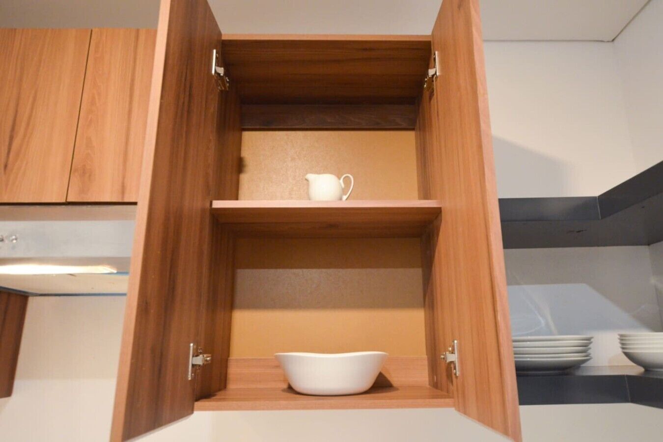 Una cocina con armarios de madera, un tazón blanco en el estante inferior y una jarra blanca en el estante superior.