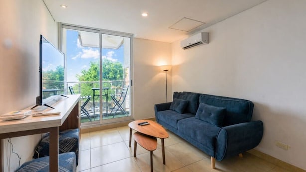 Een moderne woonkamer met een bank, een klein tafeltje, een bureau en een balkon met buitenmeubilair.