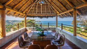 Un espace extérieur abrité, aménagé pour les repas, avec une table et des chaises, offrant une vue sur le paysage côtier.