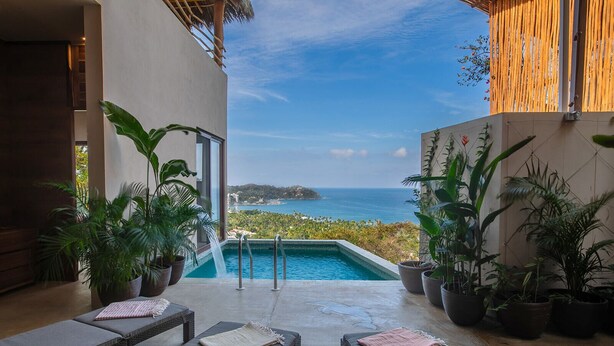 Un espace piscine aménagé avec des chaises longues, des plantes en pot et une vue sur l’océan.
