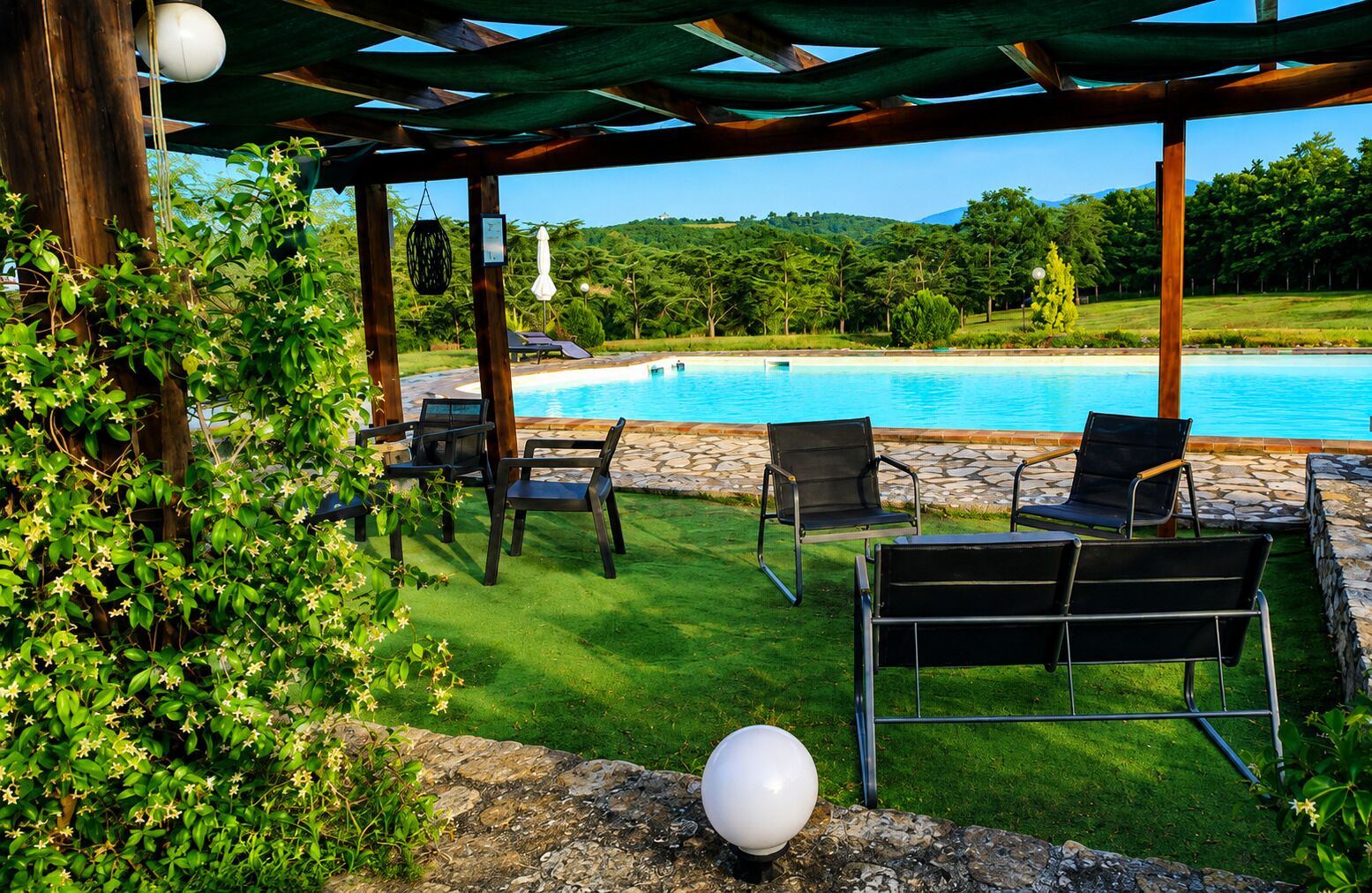 Un espace aménagé au bord de la piscine, avec des chaises et une pergola, entouré de verdure et offrant une vue sur la piscine.