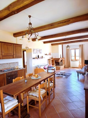 A spacious kitchen with wooden beams, a dining area with a table and chairs, and a cozy living room with a fireplace. - Caserinzio Farmhouse - Girasole: Panoramic View with Pool (avigliano umbro)