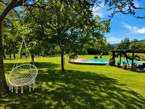Ein Garten mit Hängesessel, Schwimmbecken und einer Pergola.