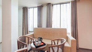 A modern living room with a sofa, two wooden chairs, a coffee table, and a window with curtains. - Super Deluxe Roomhotel Navjivan (Himatnagar)