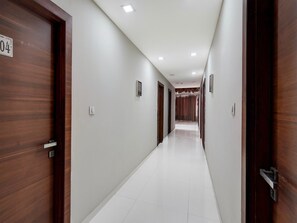 A long, narrow hotel corridor with wooden doors on either side, white walls, and a tiled floor. - Super Deluxe Roomhotel Navjivan (Himatnagar)