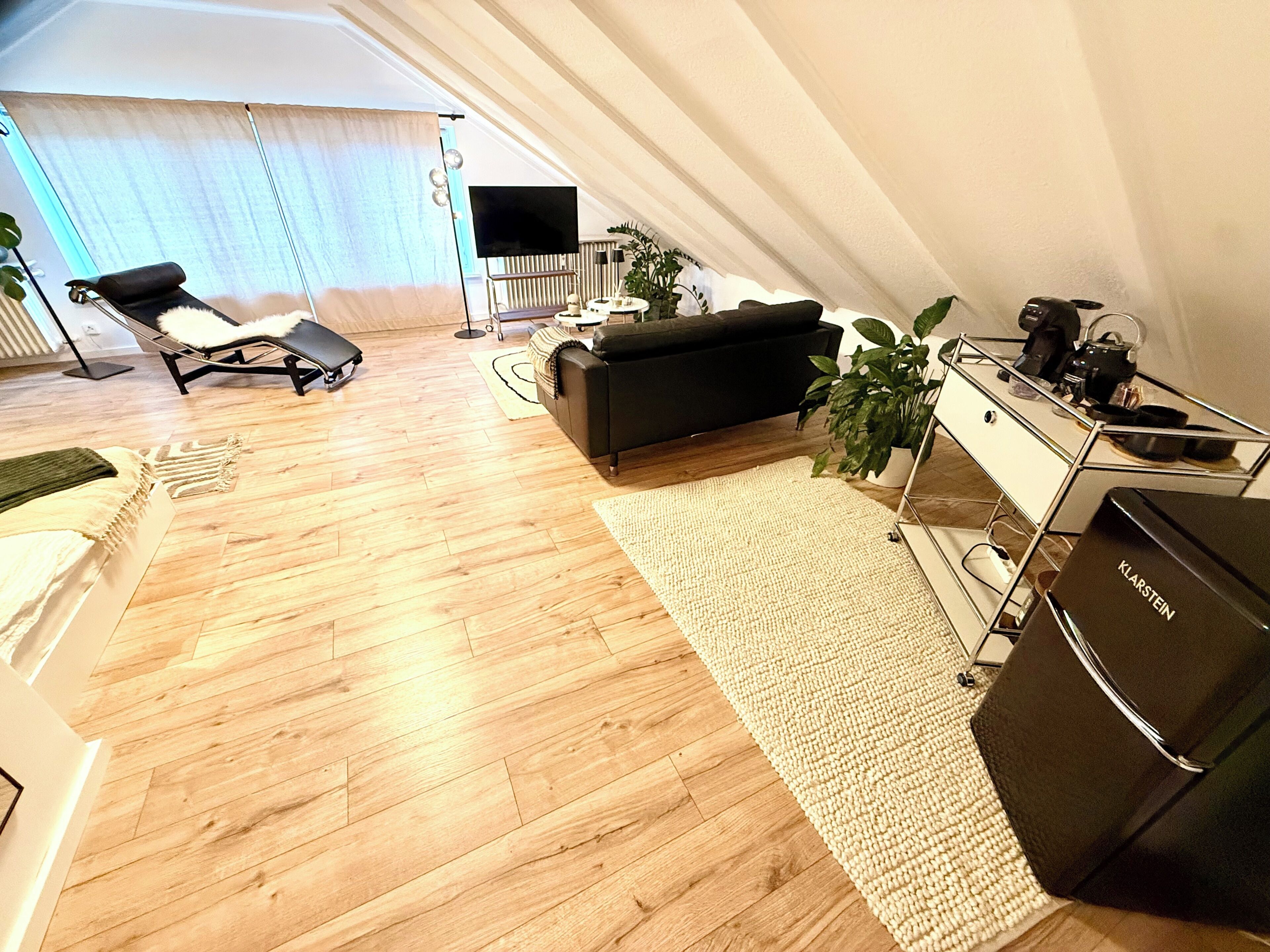 A modern living room with a sofa, a coffee table, a TV, and a kitchenette area.