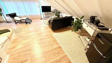 A modern living room with a sofa, a coffee table, a TV, and a kitchenette area.