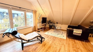 A spacious loft with a large window, a black leather chair, a black sofa, a small table, and a potted plant. - Rooftop Lounge Studio Apartment directly at the University Hospital Homburg (Homburg)
