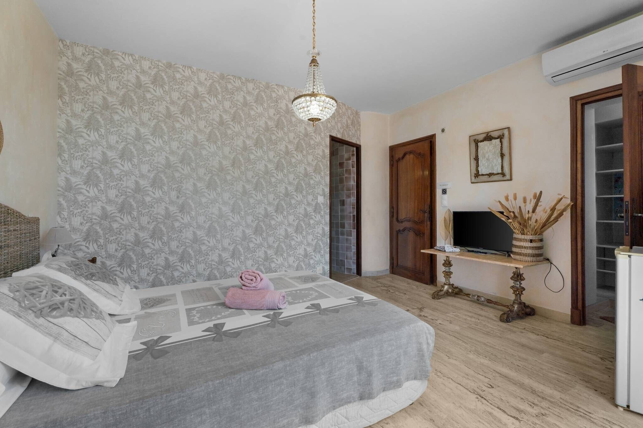Une chambre à coucher avec un lit, un lustre, une télévision et une petite table sur laquelle se trouve un vase.