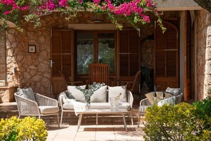 A stone building with wooden shutters, a wicker sofa set, and a table with a bottle and glasses. - Es Molí: Views, Mallorca Essence and Private pool (Santa Eugènia)