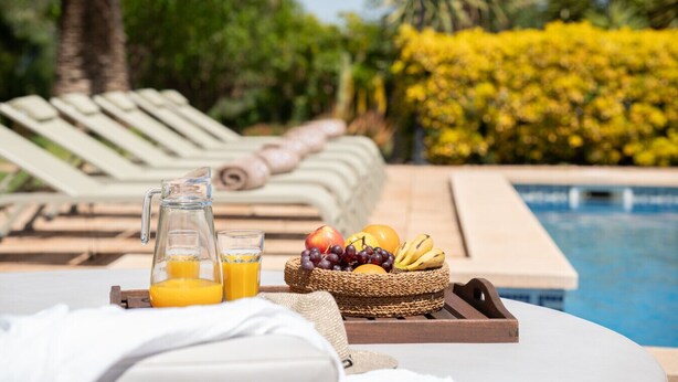Desayuno junto a la piscina con una cesta de fruta, zumo y una botella.